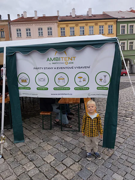 Chlapec před zeleným stanem s bannerem Ambitent na festivalu v Jičíně.