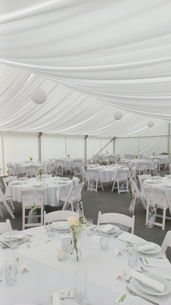 Svatební tabule v bílém stanu s kulatými stoly a květinovou výzdobou od Ambitent.